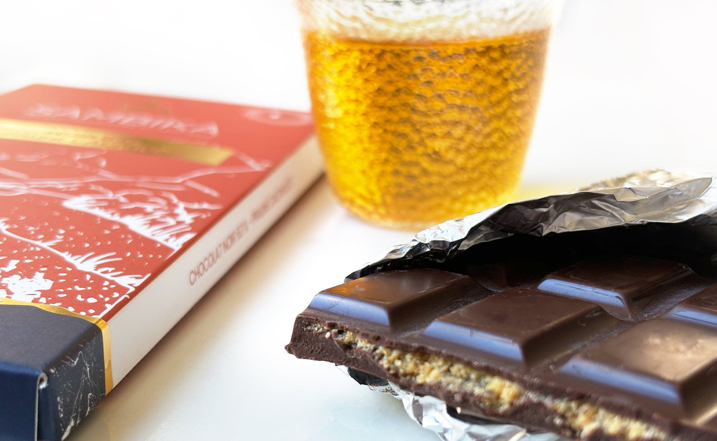 Tablette de chocolat cassée afin de montrer l'intérieur de la plaquette. La photo est également composéedu packaging du chocolat Sambika ainsi que une tasse de thé transparente avec l'accord thé - Thés des rameaux des Terrasses de l'Arrieulat 